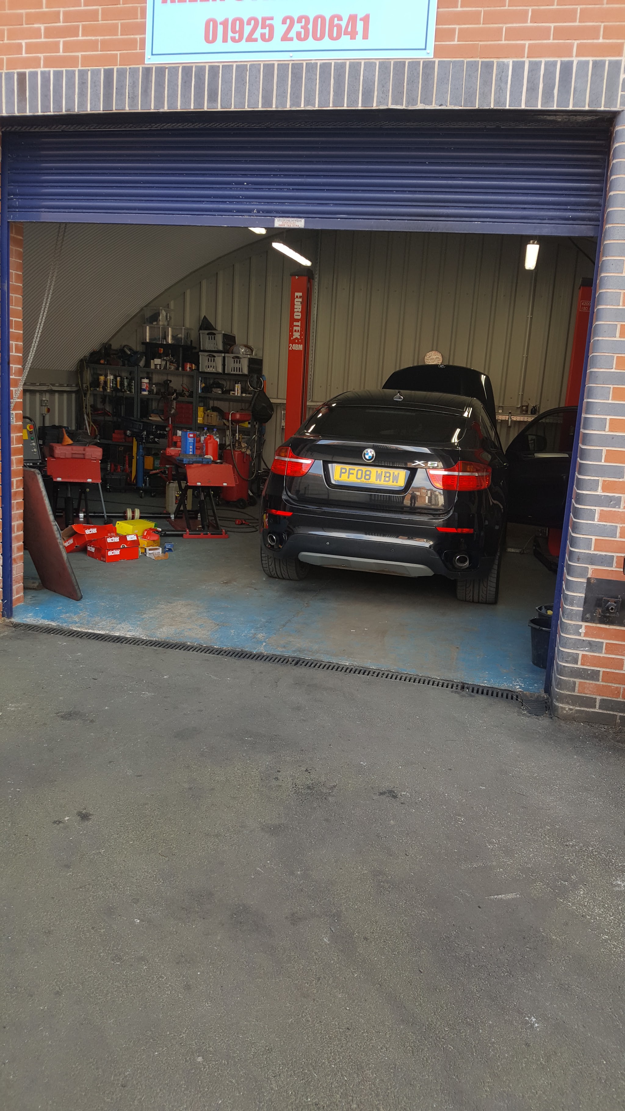 The workshop doorway with a car inside and the phone number on the sign