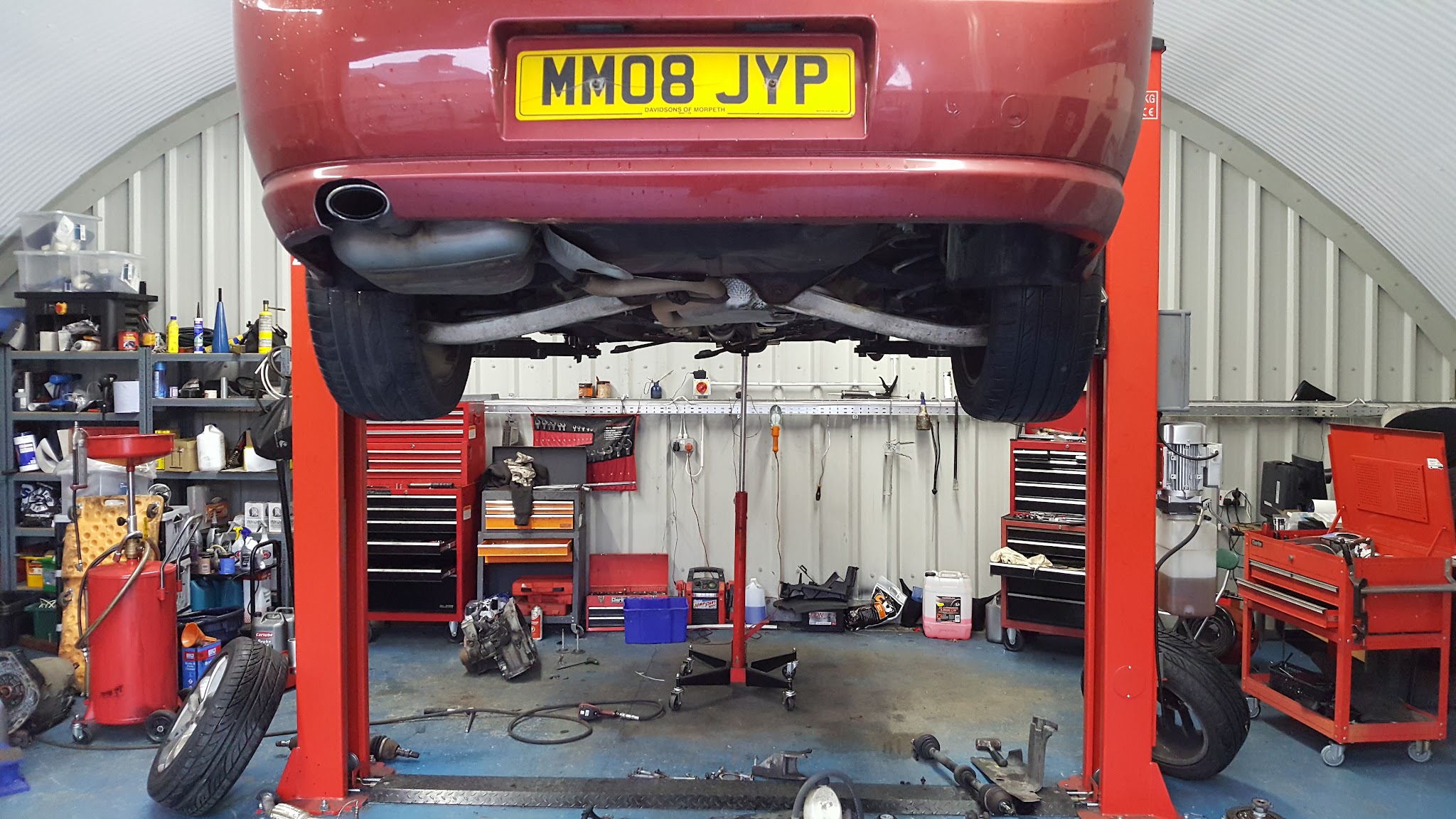 A car raised on a red two-post ramp with tools around it